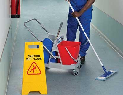 A Kenyan cleaner mopping a corridor with a cleaning trolley