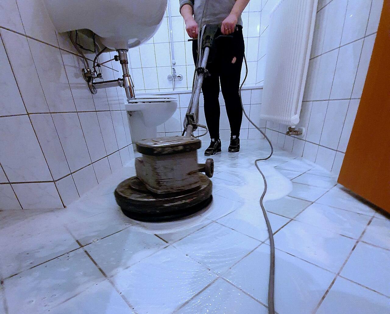 A floor-scrubbing machine deep-cleaning white floor tiles